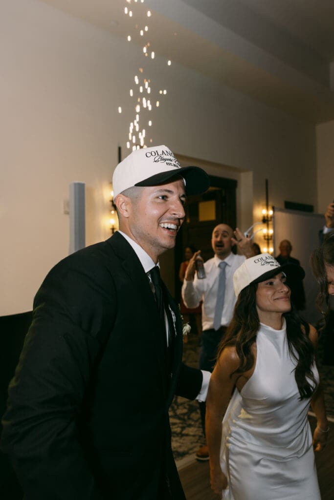 Groom laughing on the dance floor beside his bride as cold sparklers fall behind them