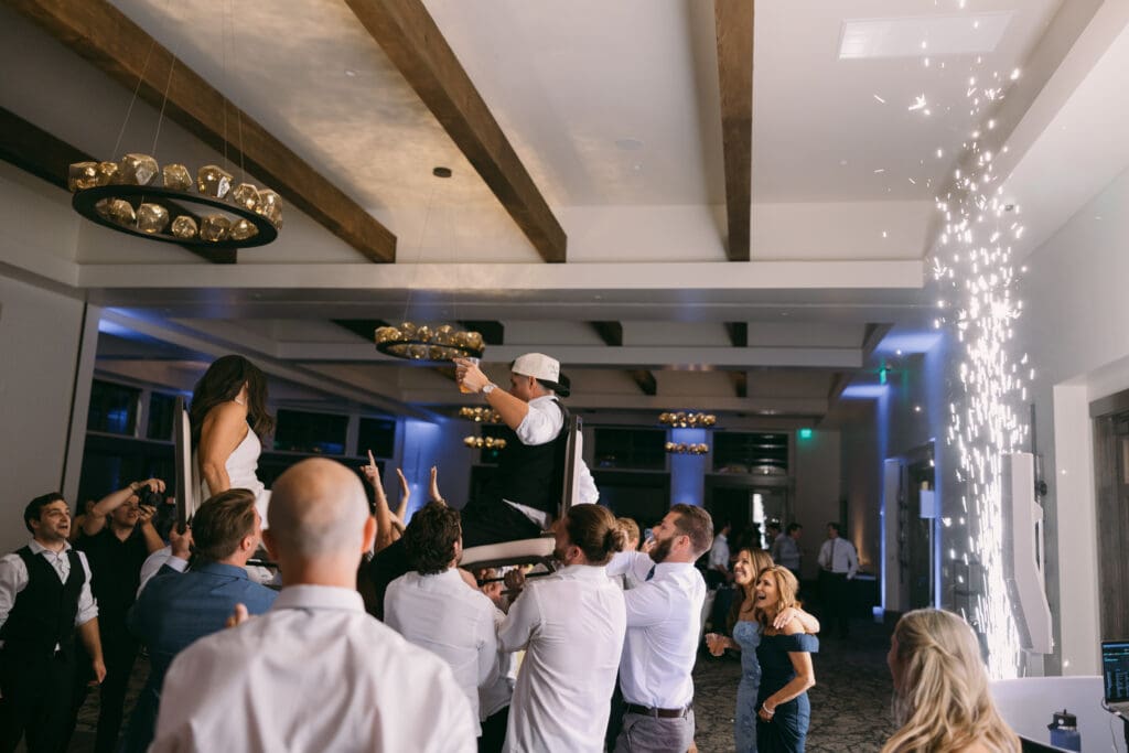 Bride lifted above the dance floor as guests cheer under cold sparklers at TPC Colorado