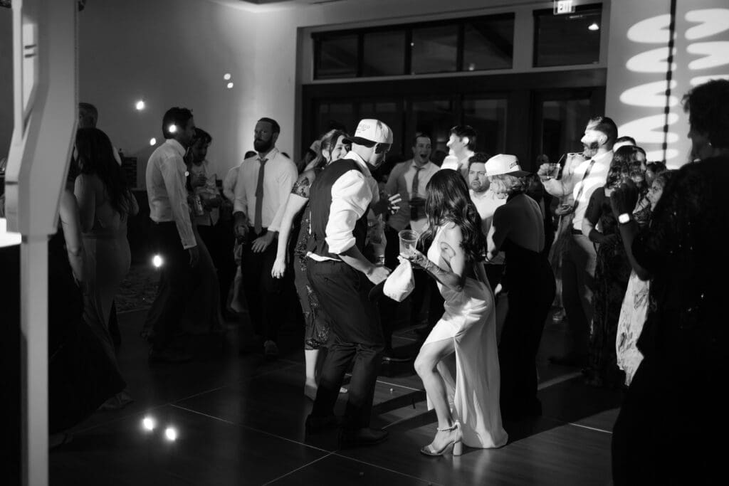 Guests in backwards ball caps dancing around the bride in black and white