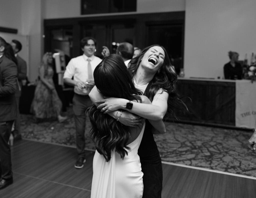 Bride hugging a friend and laughing on the dance floor in black and white