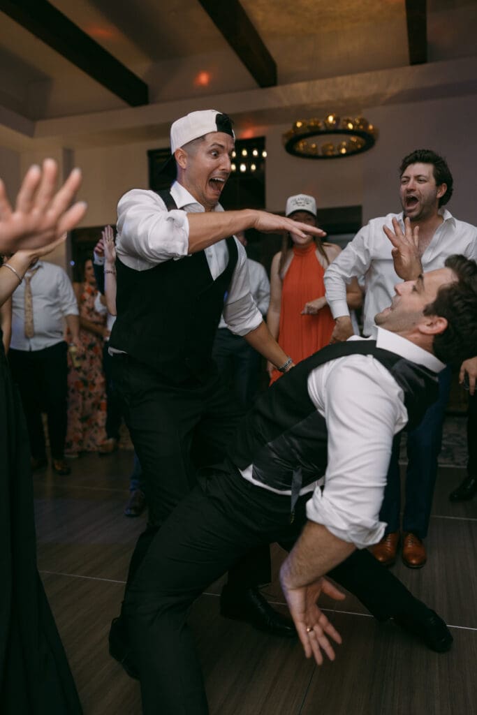 Groomsmen in ball caps and vests celebrating mid-dance during the reception
