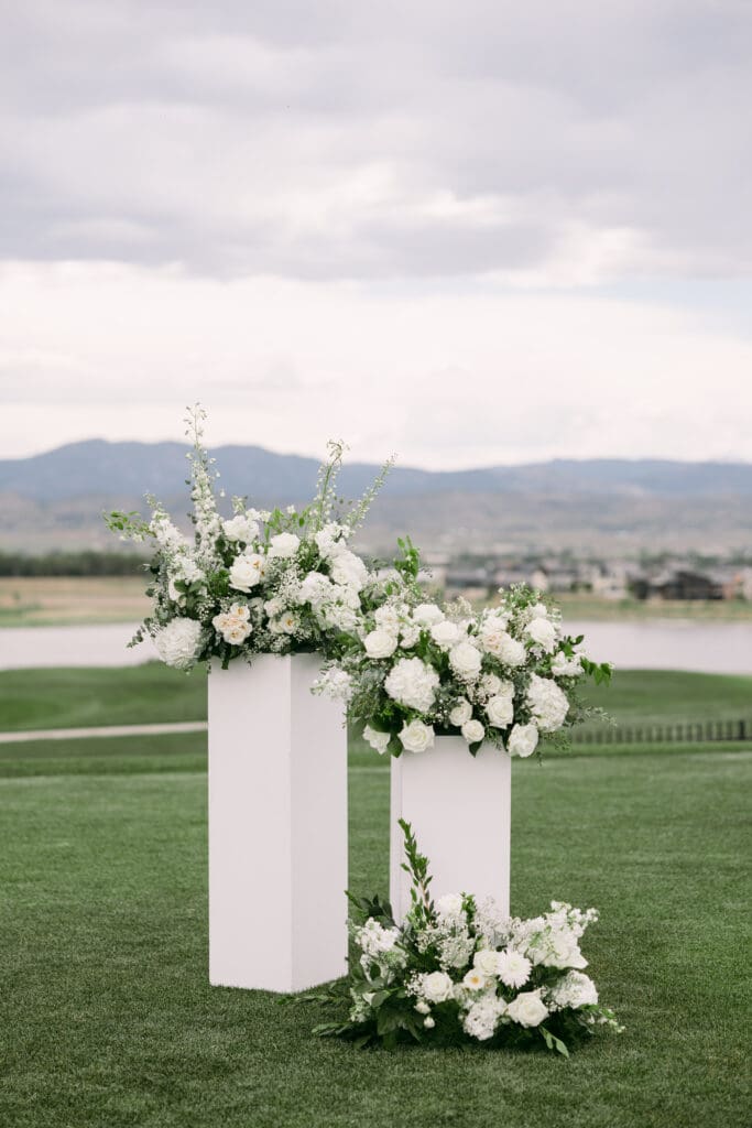 White pedestals topped with lush white florals framing the ceremony site