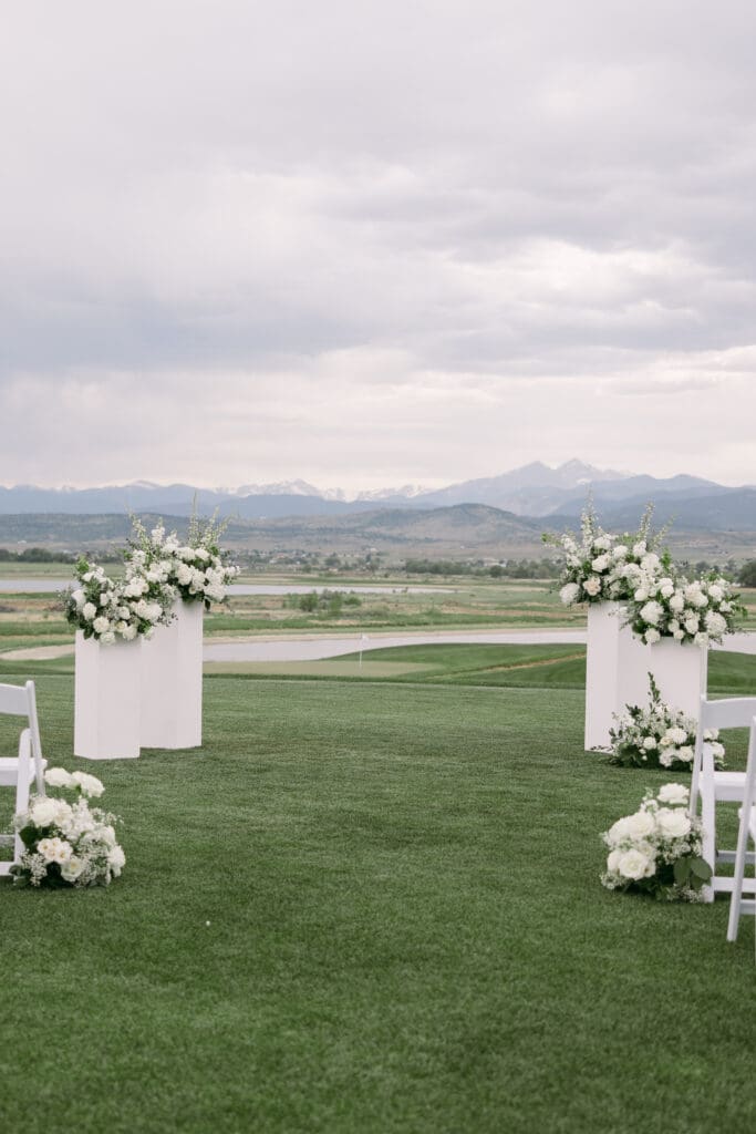 Ceremony aisle lined with white pedestals and white floral arrangements overlooking the mountains at TPC Colorado