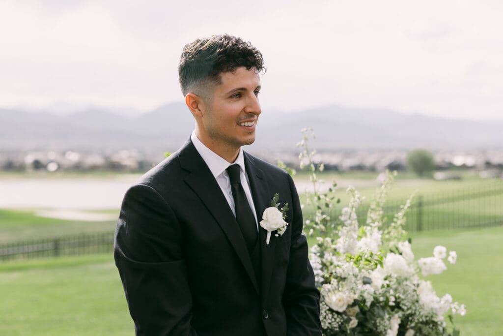 Groom smiling as he watches his bride come down the aisle at TPC Colorado