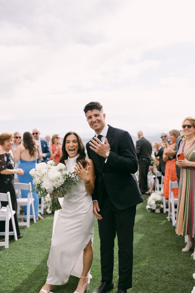 Bride laughing beside her groom as guests cheer during the recessional at TPC Colorado