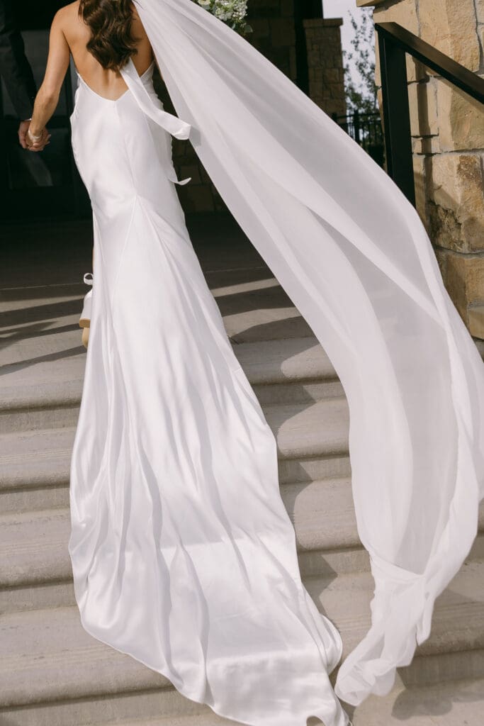Bride's sleek gown and long veil flowing down stone steps at TPC Colorado