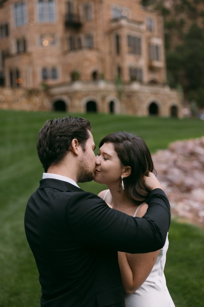 Couple kissing on the lawn with Glen Eyrie Castle softly blurred behind them