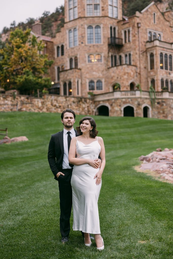 Bridgette and Logan standing close on the lawn in front of Glen Eyrie Castle