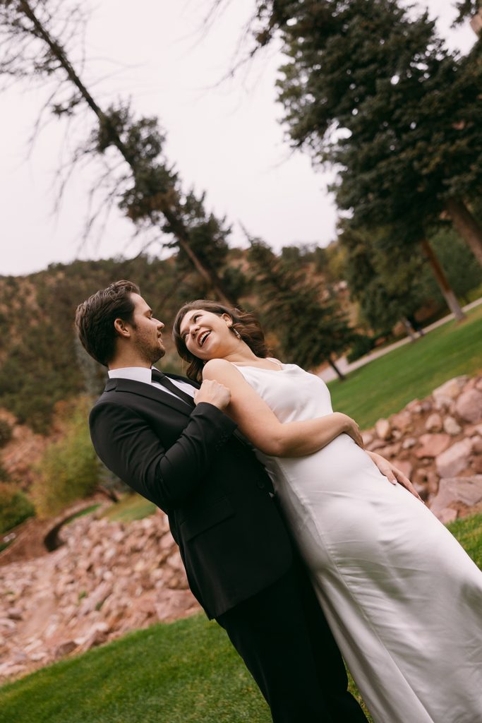 Logan dips Bridgette as they both laugh beneath the pine trees
