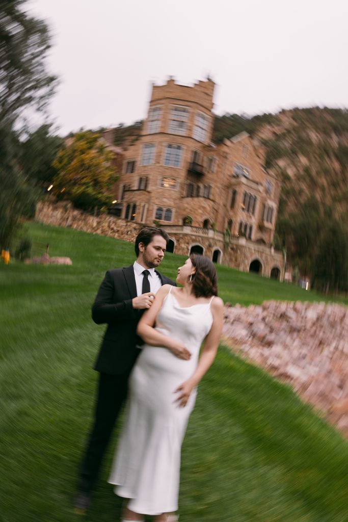 Bridgette leans back into Logan's arms on the lawn below the castle tower