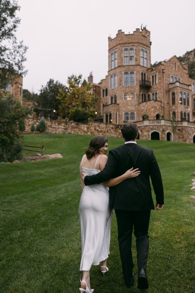 Couple walking arm in arm toward Glen Eyrie Castle across the misty lawn