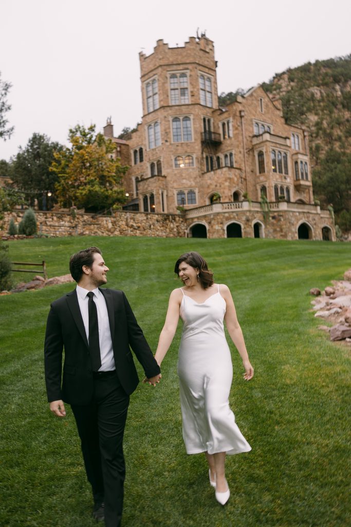 Bridgette and Logan walk hand in hand across the lawn at Glen Eyrie Castle