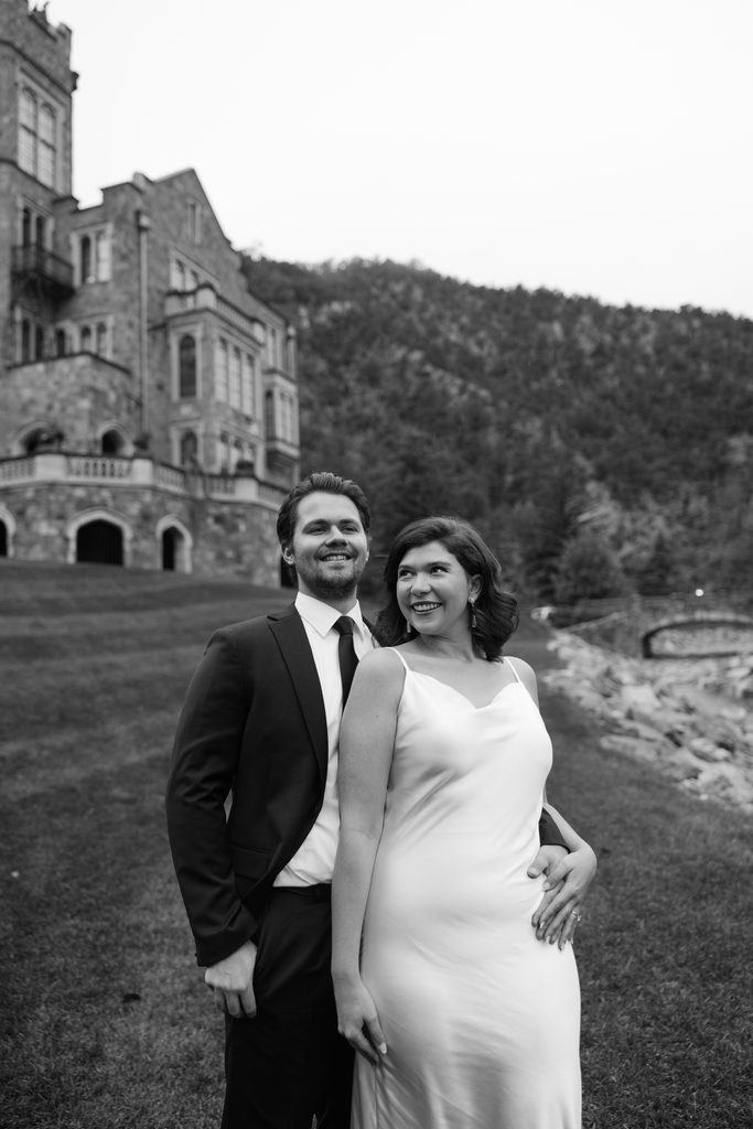 Black and white portrait of the couple laughing with the castle and foothills behind them
