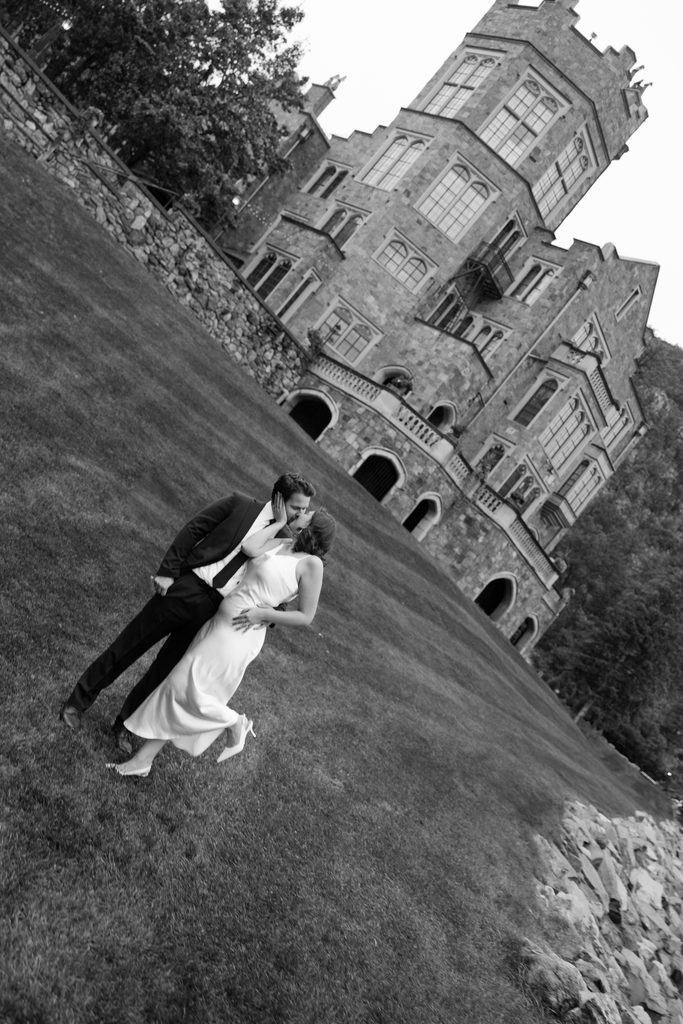 Black and white shot of the couple kissing on the hillside below Glen Eyrie Castle