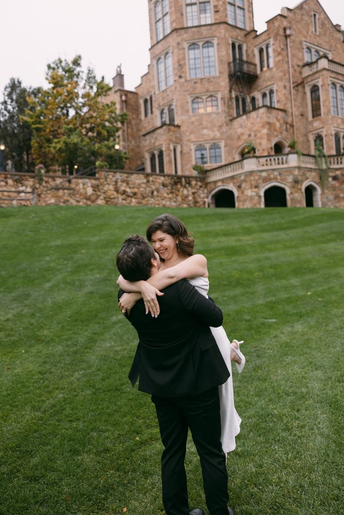Bridgette laughs as Logan lifts her on the lawn in front of Glen Eyrie Castle