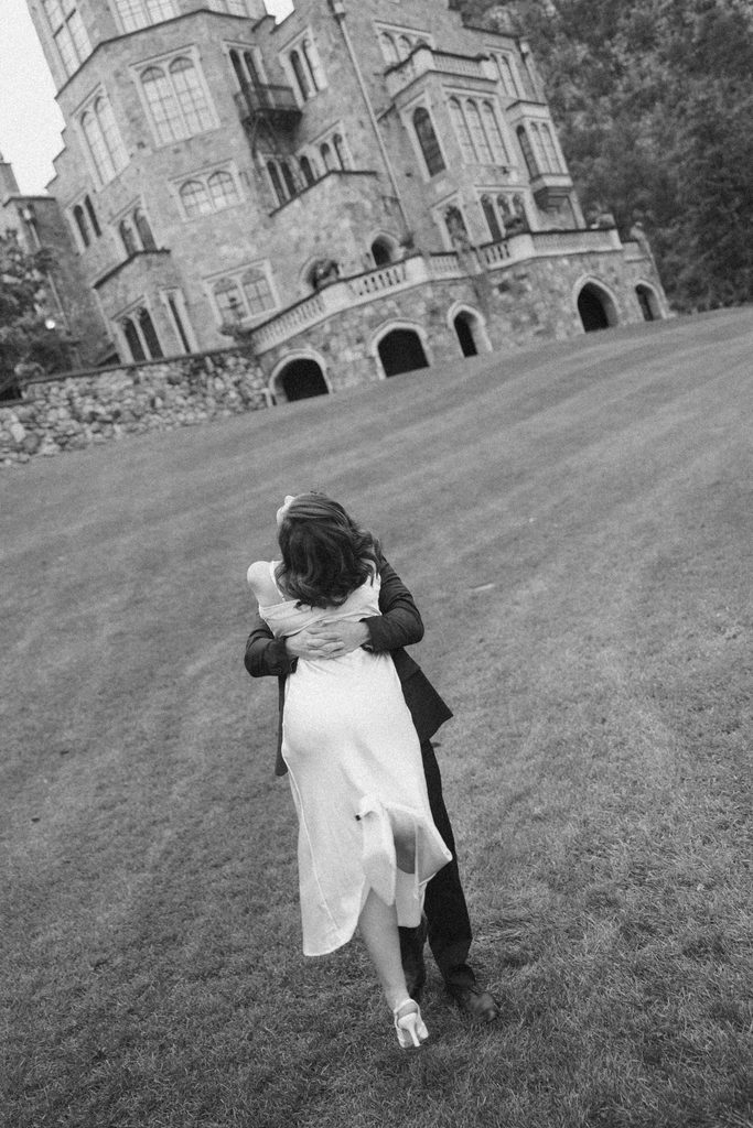 Black and white photo of Logan lifting Bridgette in a hug on the lawn below the castle