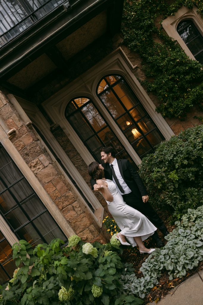 Bridgette leans into Logan beside the castle windows and greenery