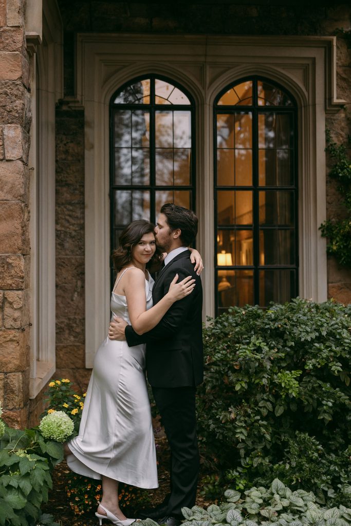 Engaged couple embracing among hydrangeas beneath arched windows