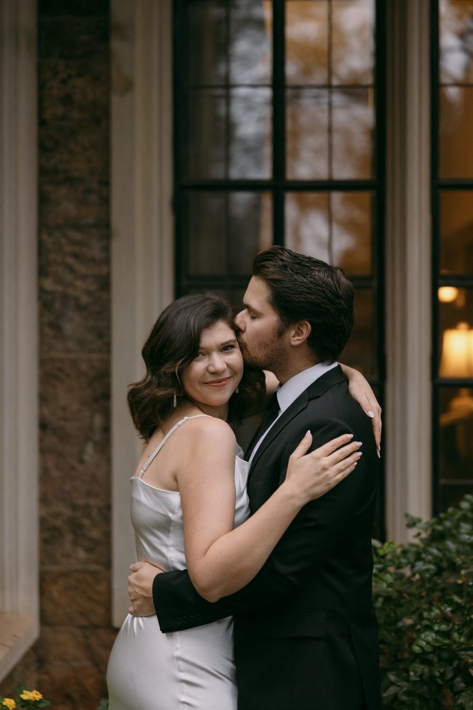 Logan leans in for a kiss as Bridgette smiles in front of the arched castle windows