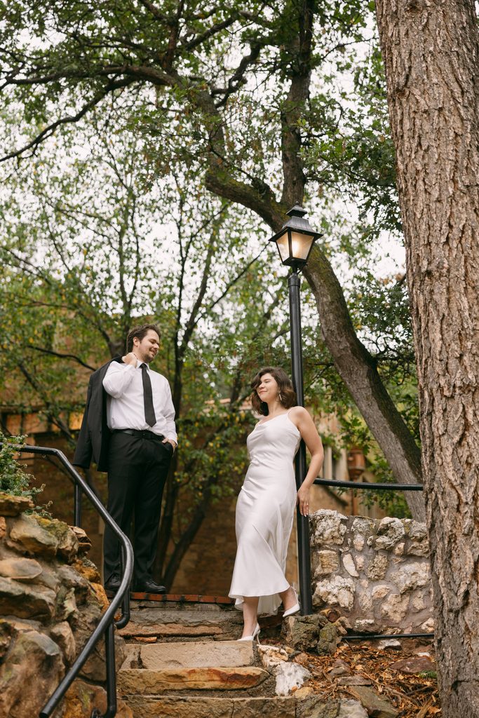 Engaged couple on stone steps beneath an old tree and lamppost at Glen Eyrie Castle
