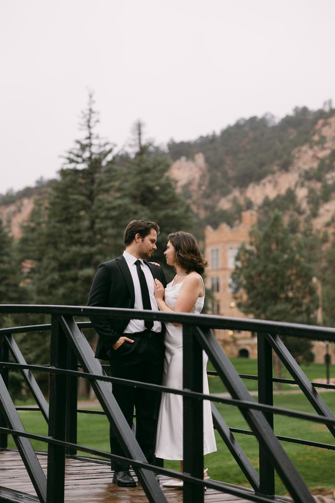 Engaged couple standing on a black iron footbridge with red rock cliffs and pine trees behind