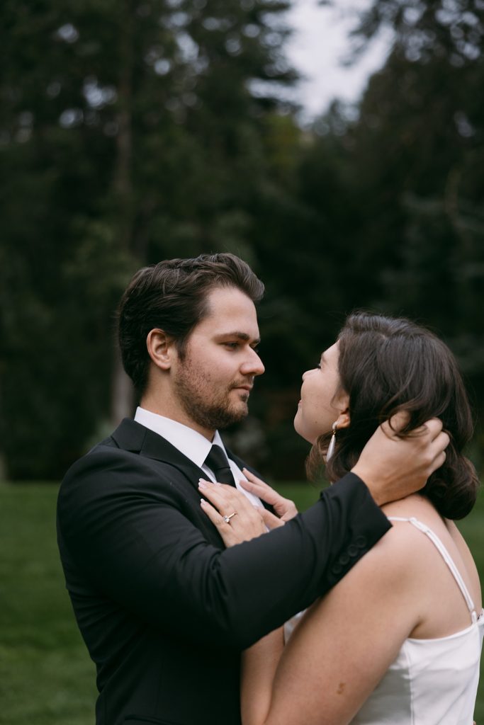 Bridgette gazes up at Logan with her hand on his neck among the pines